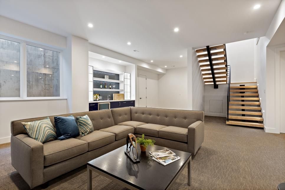Finished basement lounge with grey sectional, floating wood stairs and custom built-ins
